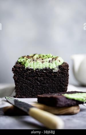 A sliced chocolate cake topped with green frosting and chocolate shavings, displayed on a wooden board with a knife nearby. Stock Photo