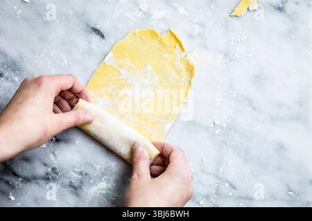 Hands rolling out dough on a floured marble surface. Stock Photo