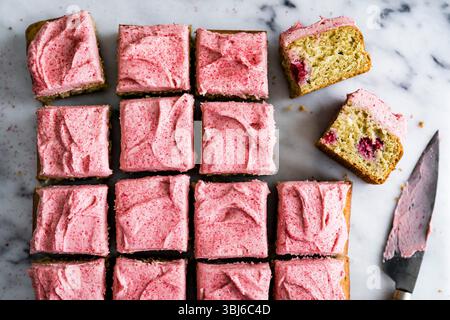 Top view of square cake pieces with pink frosting on a marble surface, one piece cut to show texture. Stock Photo
