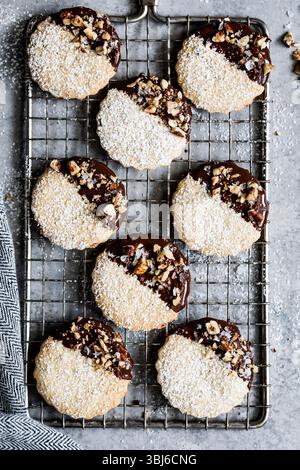 An assortment of chocolate-dipped cookies topped with powdered sugar and chopped nuts on a cooling rack. Stock Photo