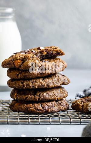 A stack of chocolate chip cookies with nuts on a cooling rack, accompanied by a jar of milk in the background. Stock Photo