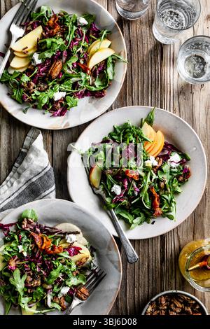 Three plates of fresh salad with apples, nuts, and greens on a wooden table. Stock Photo