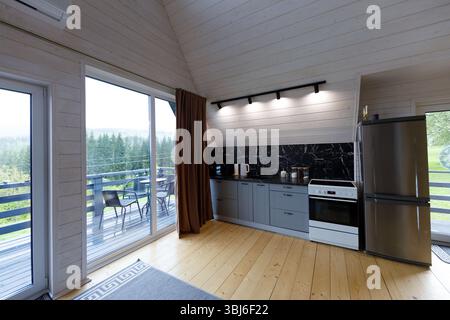 This stylish kitchen design showcases modern convenience and aesthetics, with a sleek fridge, a cozy dining area on the balcony, and beautiful natural Stock Photo
