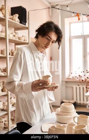 A man delicately examines a piece of pottery while surrounded by artistic creations in a studio. Stock Photo