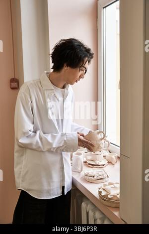 A talented man examines his ceramic creations in a bright pottery studio filled with inspiration. Stock Photo