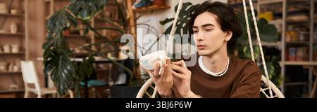 Handsome man in pottery studio thoughtfully examines his unique ceramic creation among plants. Stock Photo