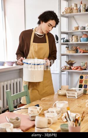 Handsome man wearing an apron carefully examines pottery materials in a vibrant studio Stock Photo