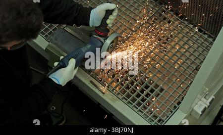Overhead view of angle grinding metal with bright sparks. A top-down view of a person using a handheld angle grinder to cut through a metal plate on a Stock Photo