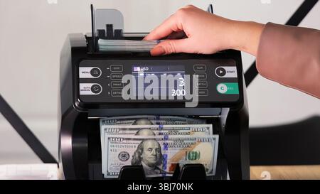 Hand placing US dollars into an electronic money counter. A close-up view of a person inserting a stack of US dollar bills into a digital currency Stock Photo