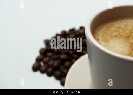 Freshly brewed coffee in a white cup sits on a saucer with roasted coffee beans scattered nearby, creating a cozy and inviting scene Stock Photo