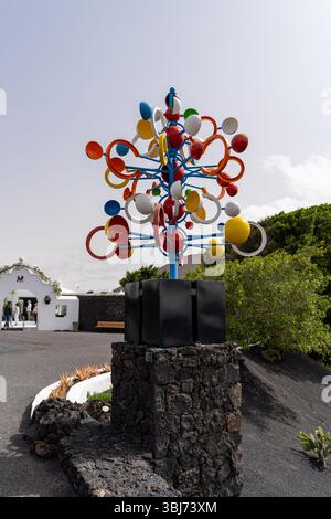 A vibrant sculpture at the Cesar Manrique Foundation in Lanzarote, showcasing colorful art against the bright sky and a traditional building. Stock Photo