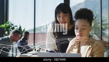 Collaborating business professionals leaning over laptop in office meeting room, with coffee mugs Stock Photo