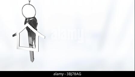 Hanging silver keyring swaying on white backdrop with metal keys and house-shaped charm, copy space Stock Photo