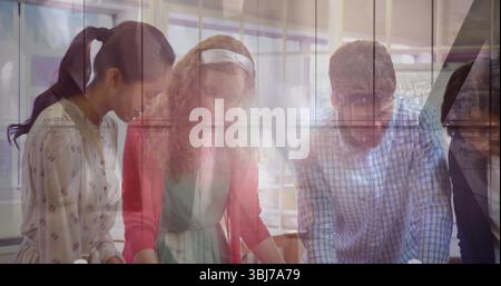 Leaning over blueprints three colleagues collaborating in meeting room with wooden table and pens Stock Photo