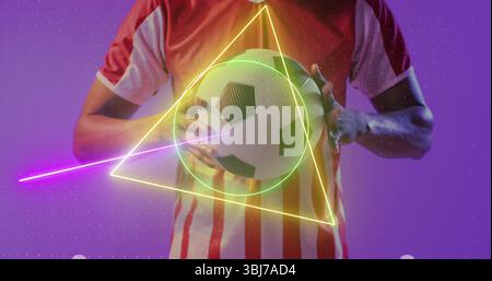 Posing man wearing striped soccer jersey holding soccer ball in studio, with neon geometric shapes Stock Photo