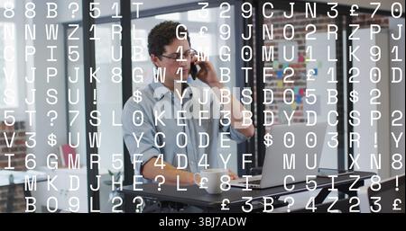Talking office worker using smartphone and checking laptop at desk, with whiteboard and coffee mug Stock Photo