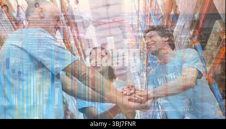 Three light blue T-shirt volunteers joining hands in warehouse aisle with shelving and boxes Stock Photo