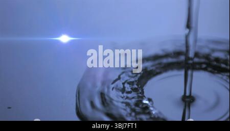 Pouring water stream creating ripples on reflective surface in studio, with lens flare, copy space Stock Photo