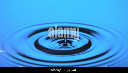 Capturing water droplet creating concentric ripples on reflective water surface in studio Stock Photo