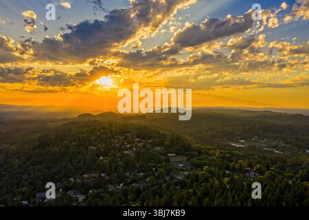 Portland, Oregon - June 12th 2019: Sunset over the West Hills. The sun's rays stream through the clouds, illuminating the landscape and the city below Stock Photo