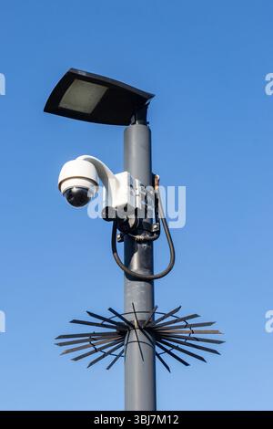 CCTV camera mounted on a pole with bird spikes and solar panel against a clear blue sky Stock Photo