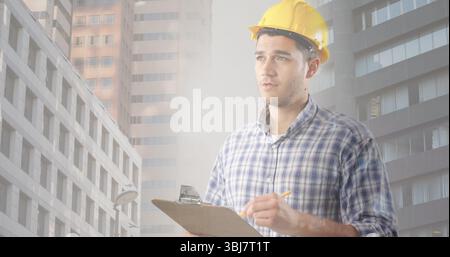 Inspecting engineer wearing hard hat taking notes on clipboard in downtown construction Stock Photo
