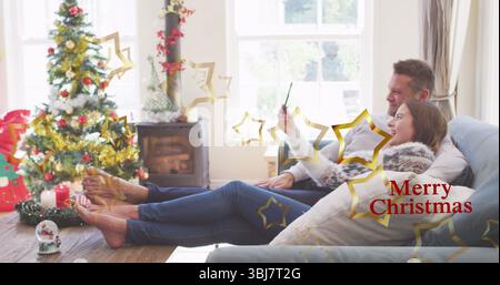 Reclining couple in sweaters taking selfie in Christmas living room, with tree, stove, copy space Stock Photo