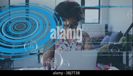 Woman in floral top focusing on laptop coding apps in modern office, with notebooks, 5G overlays Stock Photo