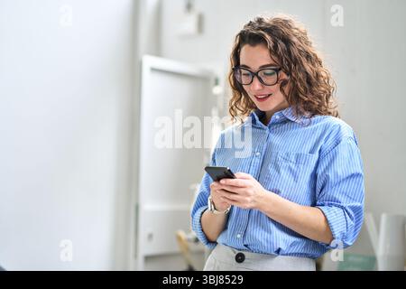 Happy young business woman using cellphone standing in office using mobile. Stock Photo
