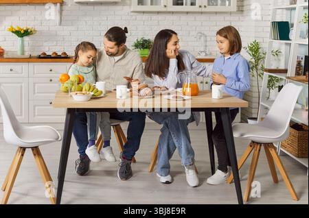 Happy family spending morning together in kitchen, enjoying fresh breakfast with pastries and juice. Stock Photo