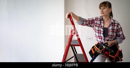 Woman doing home renovation with her hands holding drill standing on ladder indoor. banner, copy space Stock Photo