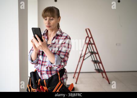DIY home renovation concept. Woman using smartphone reading social media using mobile phone apps renovating her home. Copy space Stock Photo