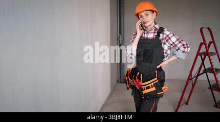 Female builder calling on smartphone indoors room with building background. profession, renovation, construction and repair concept Stock Photo