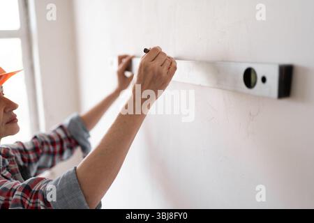 Female builder or construction worker measures wall in new house with a spirit level. Stock Photo