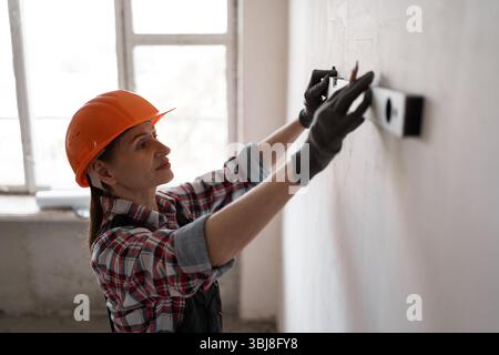 Repair and construction concept. Female engineer or builder in helmet measures level of wall in a house checking it Stock Photo