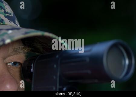 A man in a pixel camouflage cap takes aim with a shotgun. The theme is hunter, soldier or sniper in action Stock Photo