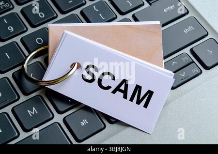 SCAM text on white notepad with laptop keyboard background. Hacker and scam activity concept Stock Photo