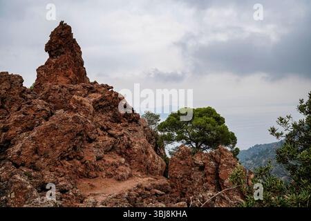 A narrow dirt path winds through rugged lava rock formations and dry brush on the volcanic slopes of Kameno Vouno in Methana. Stock Photo