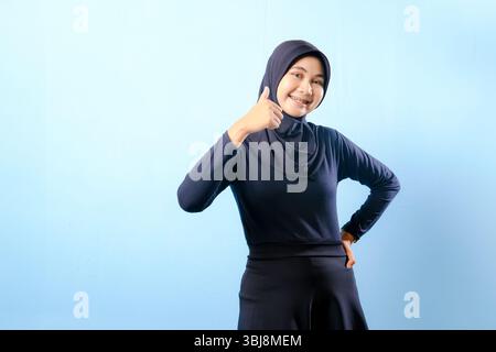 A woman wearing a black dress and a black head scarf. She is smiling and giving a thumbs up Stock Photo