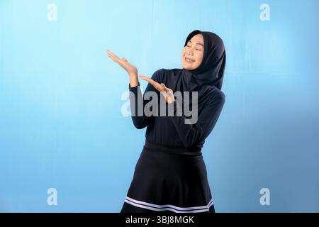 A woman wearing a black skirt and a black head scarf. She is pointing towards something. She is smiling Stock Photo