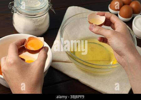 Woman separating egg yolk from white over glass bowl at table, closeup Stock Photo