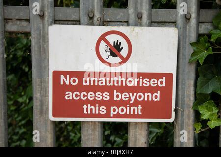 “No unauthorised access beyond this point” sign on a rural path with dense green trees in the background, indicating restricted entry. Stock Photo