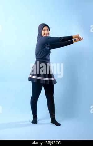 A woman in a black outfit is stretching her arms out to the side. She is wearing black socks and black pants Stock Photo