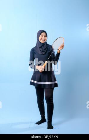 A woman in a black skirt and black pants holding a badminton racket. She is smiling and she is happy Stock Photo