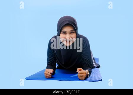 A woman in a black hijab is lying on a blue mat. She is smiling, and she is enjoying herself Stock Photo