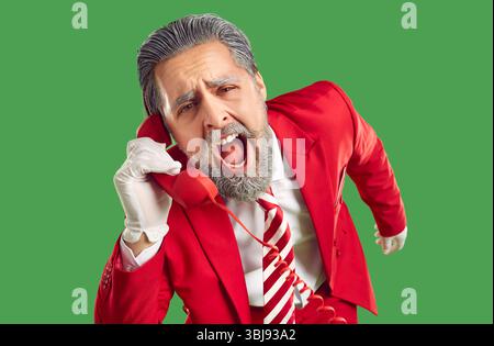 Positive, extravagant, stylish, young Santa Claus, dressed in classic stylish red suit, screams with his mouth open into the phone receiver. Stock Photo