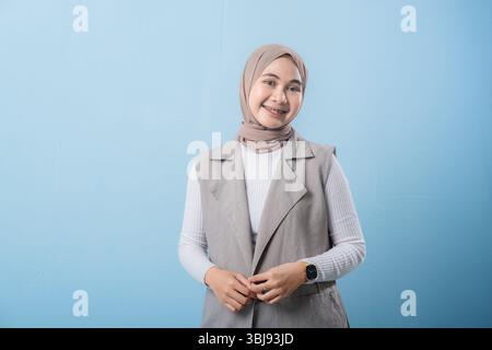 A woman wearing a white shirt and a tan scarf stands in front of a blue wall. She has a smile on her face and she is happy Stock Photo