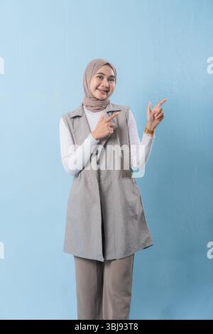 A woman wearing a grey vest and a white shirt is pointing to something important. She has a smile on her face and is wearing a turban Stock Photo