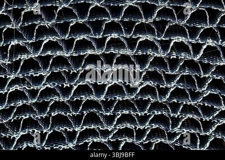 Detailed close-up of metal mesh fabric with a repeating wavy pattern, showing texture, structure, and light reflections, used for shading, fencing Stock Photo
