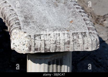 Close-up of an old stone bench with a rough, weathered surface and carved edge pattern, revealing aggregate and signs of age, set outdoors in natural Stock Photo